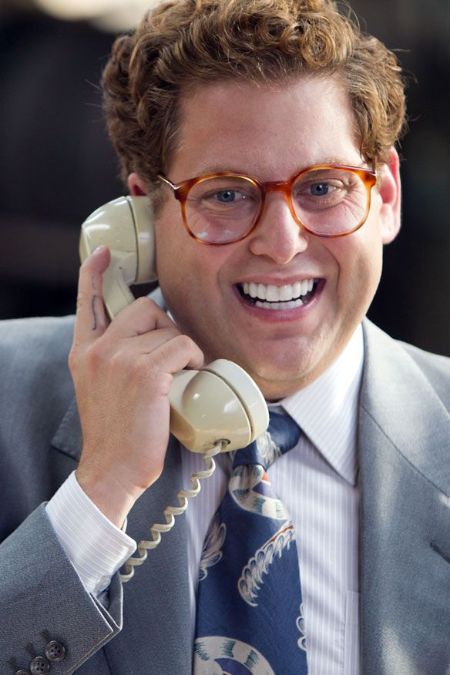 Jonah Hill in a grey suit holding a telephone while shooting.